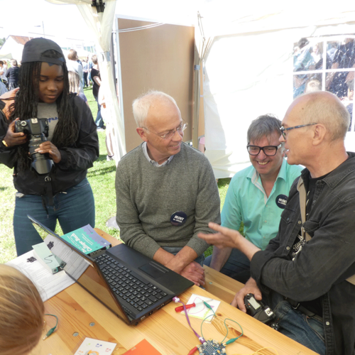 Gespräch zwischen 3 älteren Männern vor einem Laptop, ein junger Mann hört zu